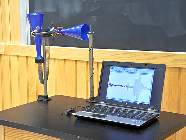 A computer-interfaced microphone is supported by a ringstand at one end of the space phone. A chirp waveform is visible on the monitor.