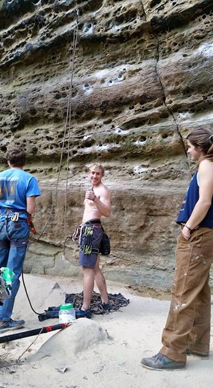 A climber on the ground, strapped in, making a thumbs-up sign at the camera 