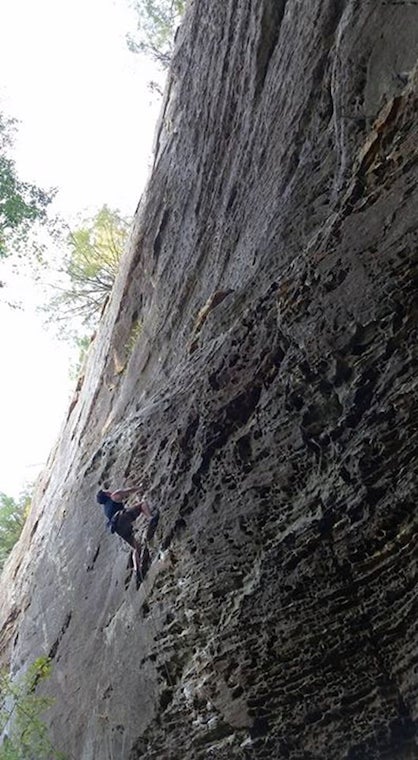 A climber ascending a very steep natural wall 