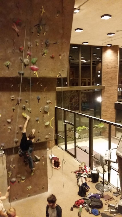 A climber, harnessed, ascends a wall as other onlook