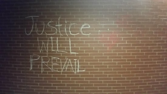 A brick wall with the words "justice will prevail" chalked on the wall 
