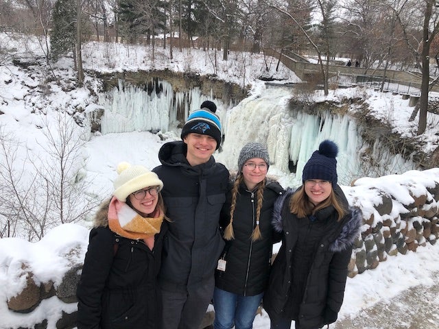 Ilana, Drew, Ciara, and Makaela stand in front of Minnehaha Falls, a frozen waterfall, in full winter gear