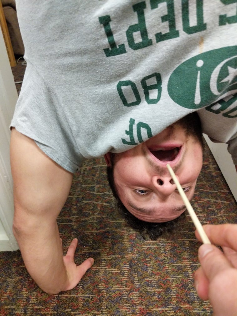 A chopstick is seen close to Teague's mouth, as he attempts a handstand
