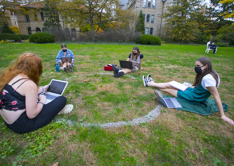 A small group of students sit in a circle on the grass.