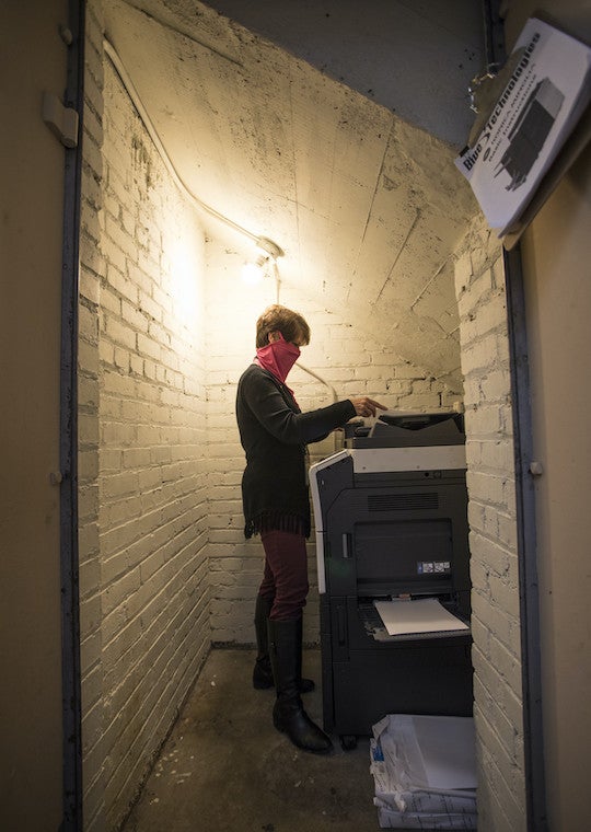 A woman makes copies from a machine located in a small walk-in safe.