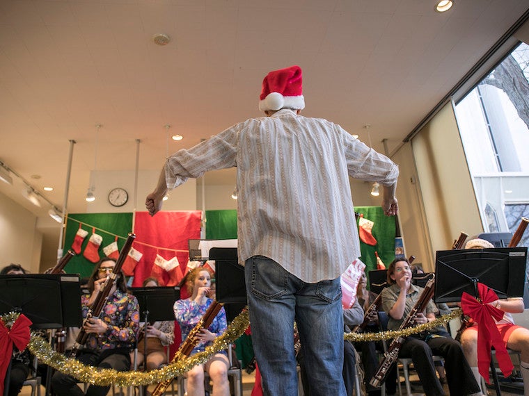 A conductor wearing a Santa Claus hat leads a bassoon orchestra.