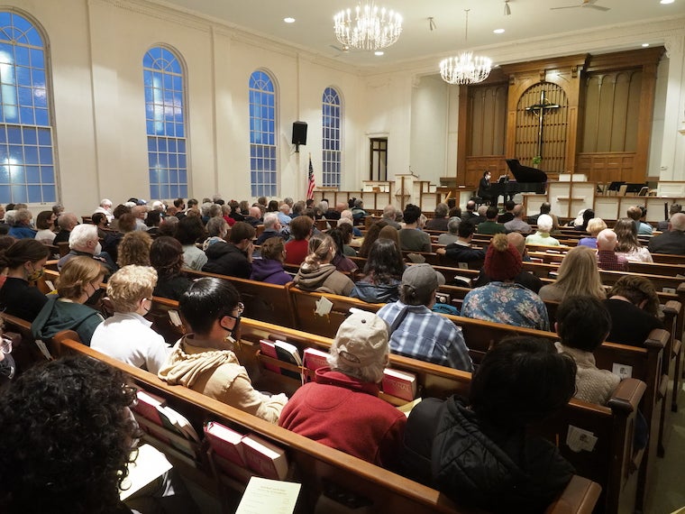 A large audience in a church listens to a man playing piano