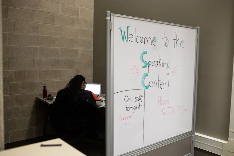 A whiteboard has a handwritten message: Welcome to the speaking center! Hours: Su, T, Th 7-9 pm. On staff tonight: Carrie.