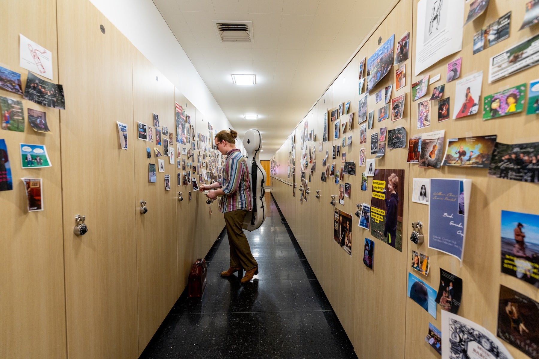 Person standing in a hallway lined with wooden walls, covered in photos, postcards, and artwork.
