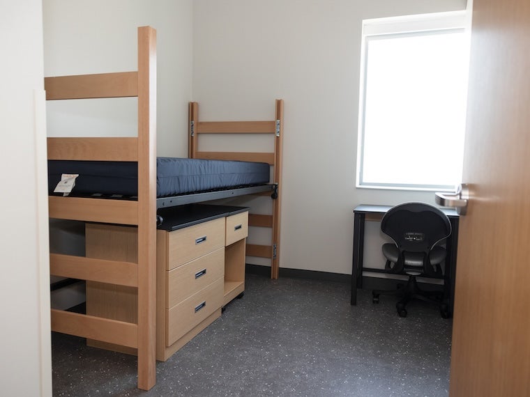 Dorm room with a loftable bed, desk, chair, and window.