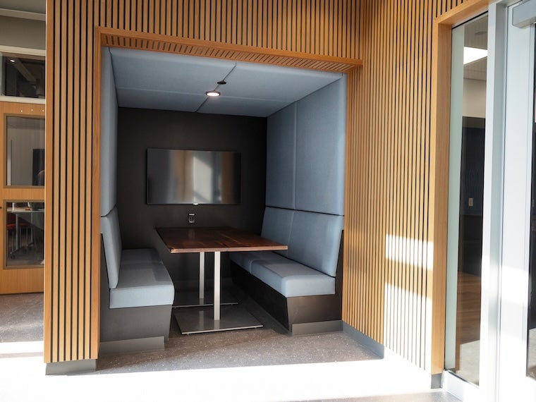 Modern booth seating area with a wooden table and cushioned benches, enclosed by wood paneling.