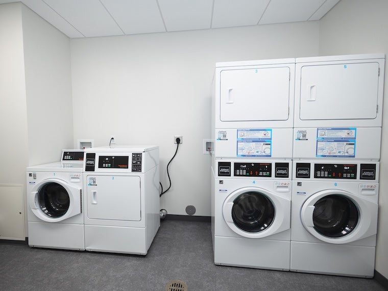 Laundry room with front-loading washers and dryers against a white wall.