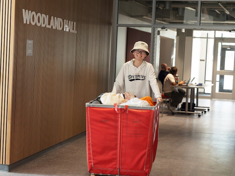 happy student pushing a cart through a residence hall entryway.