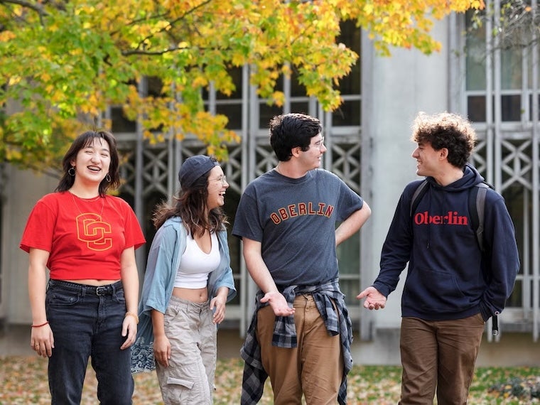 Four students walk together outside in autumn, laughing and wearing Oberlin apparel.