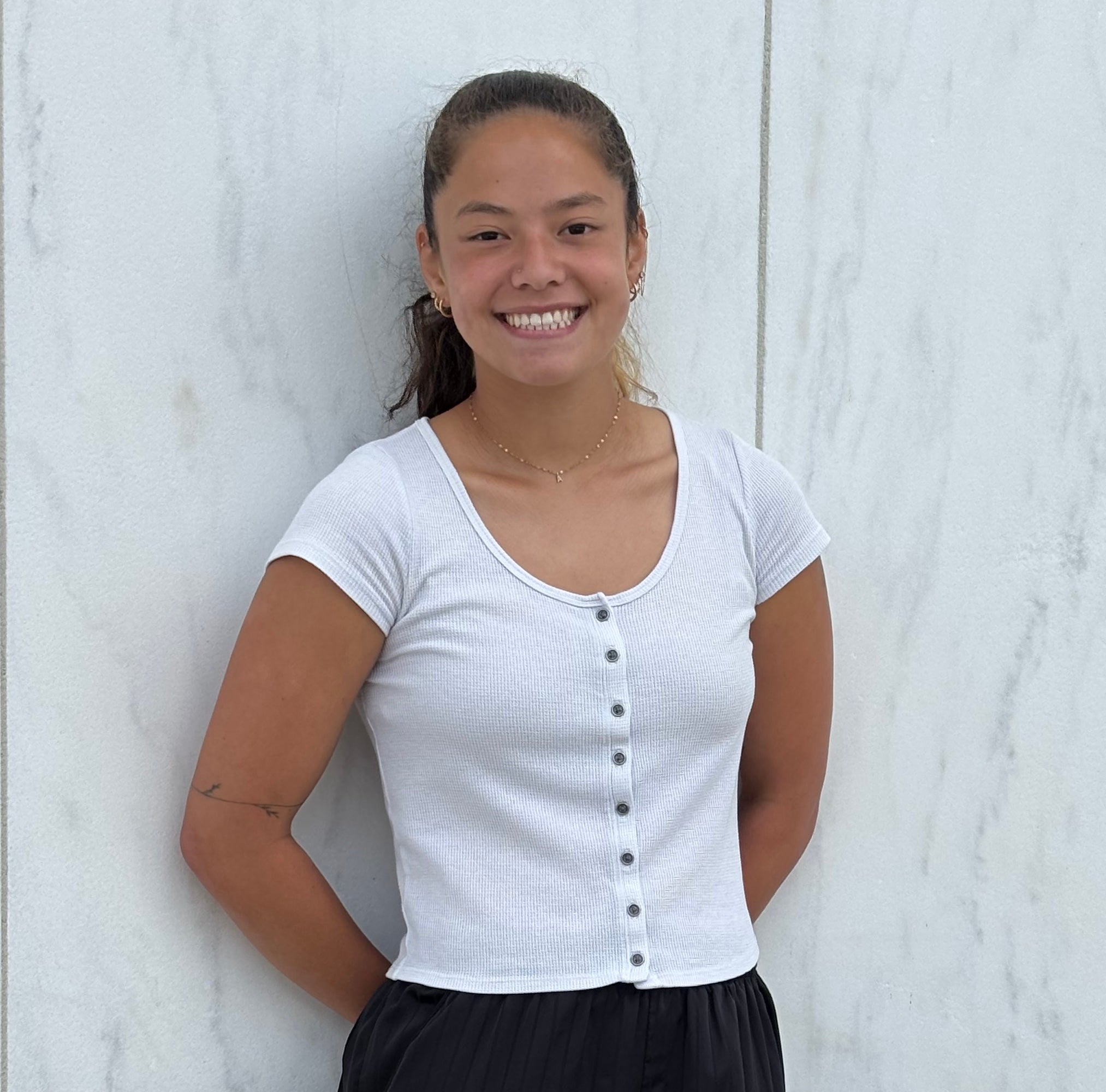 A female Oberlin student in a white shirt, standing in front of a white wall.