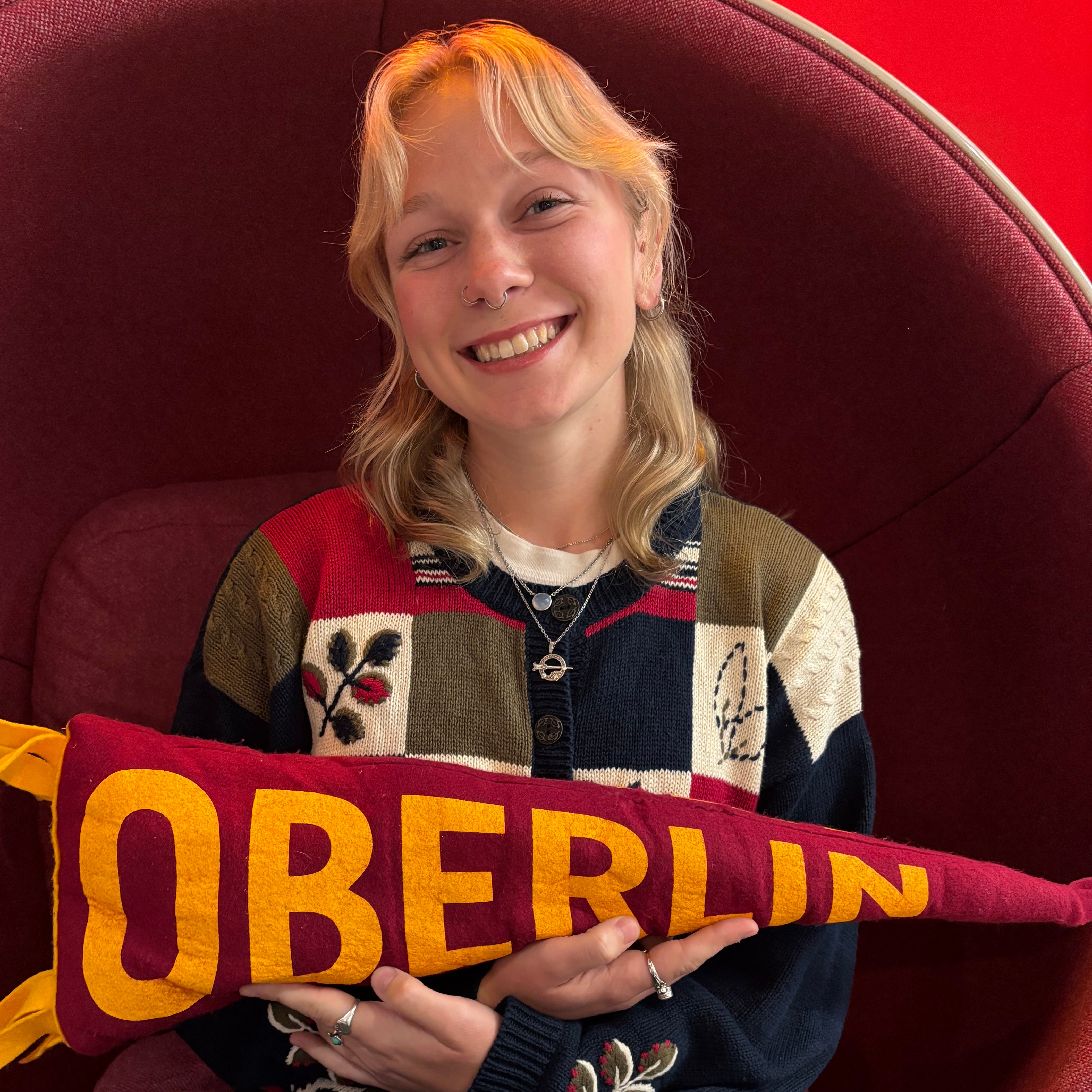 An Oberlin student with blonde hair sitting in a red chair.