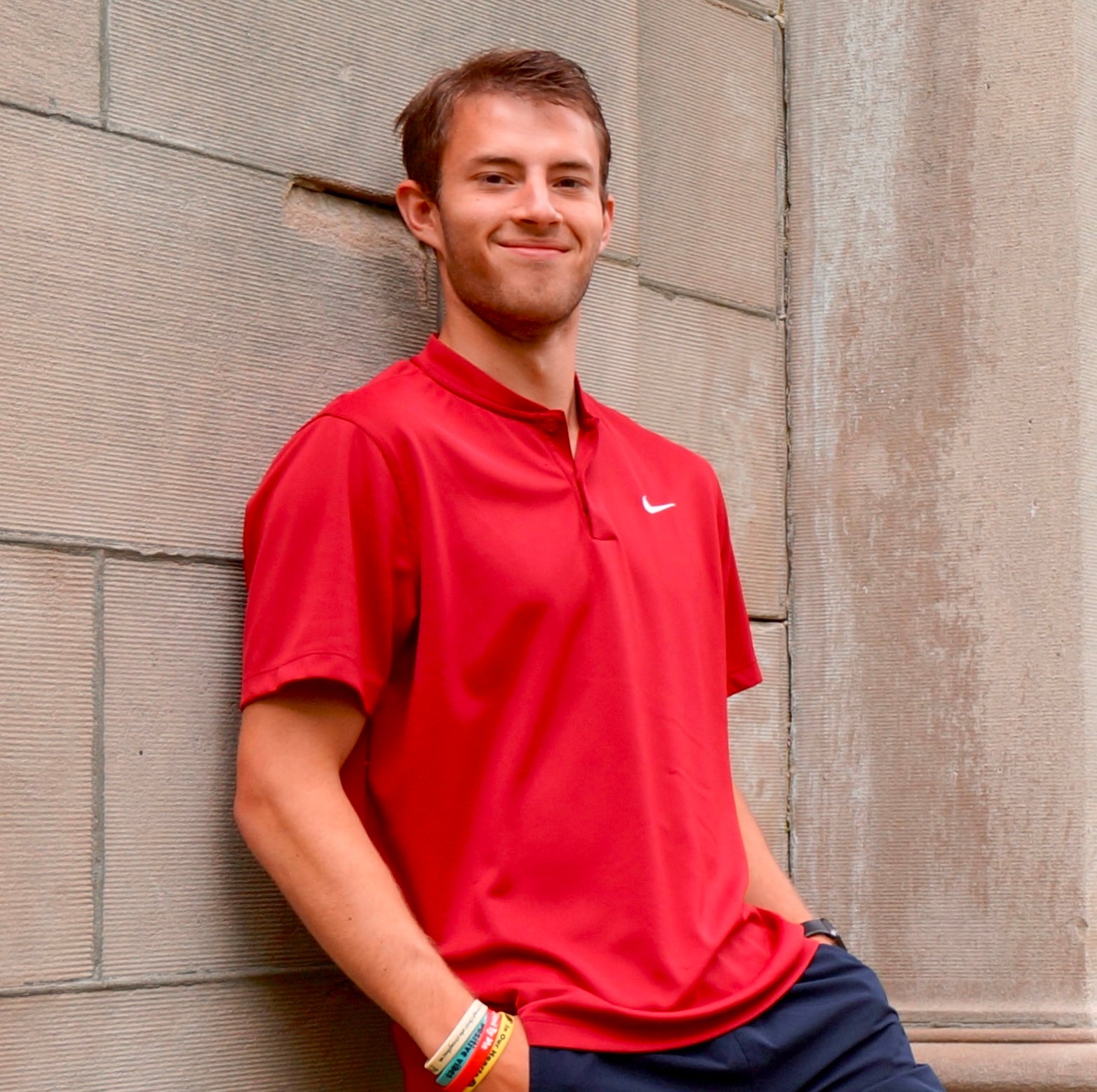 A male Oberlin student in a red shirt, standing against a wall.