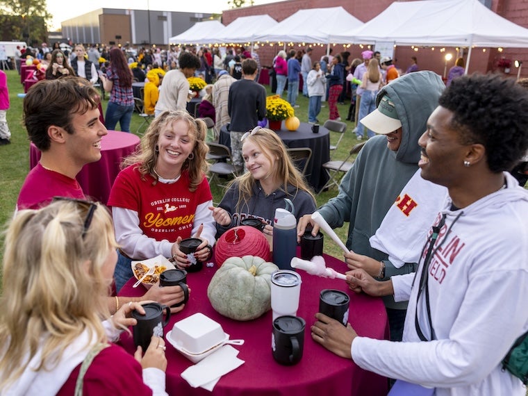 Students talk and smile around a table at an outdoor campus event.