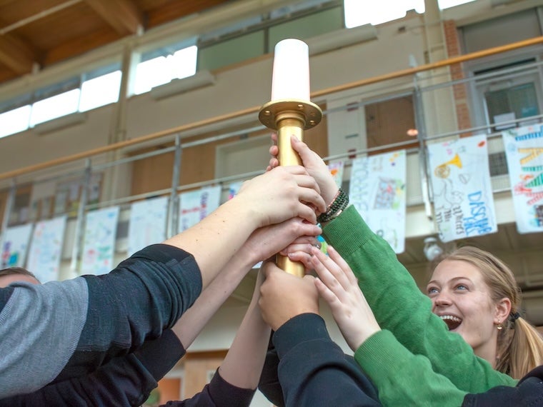 Group of students raising an Ecolympics torch together indoors.