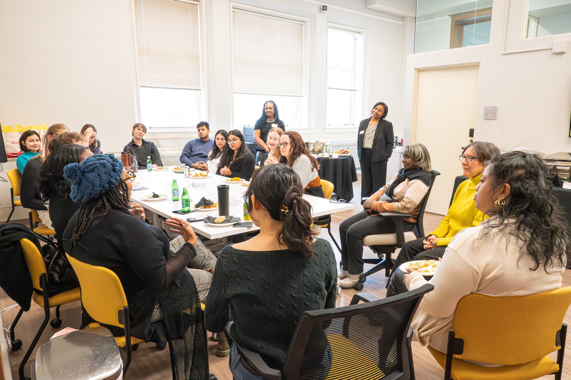 Group of students and staff seated in a circle during a facilitated discussion in a meeting room.
