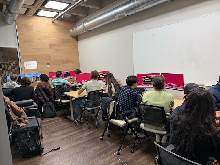 Students seated at tables using desktop computers during a workshop in a classroom.