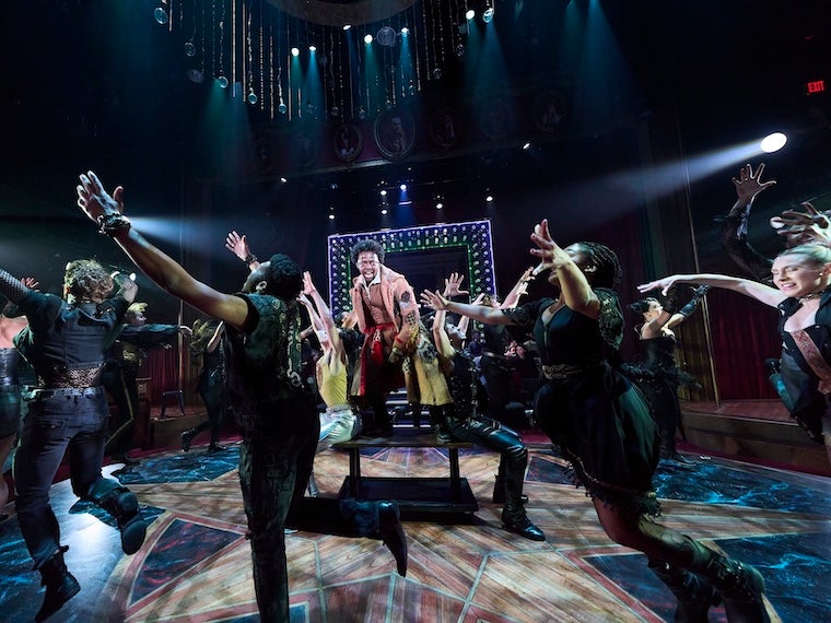 Music theater students rehearsing a high-energy dance number onstage under dramatic blue lighting.