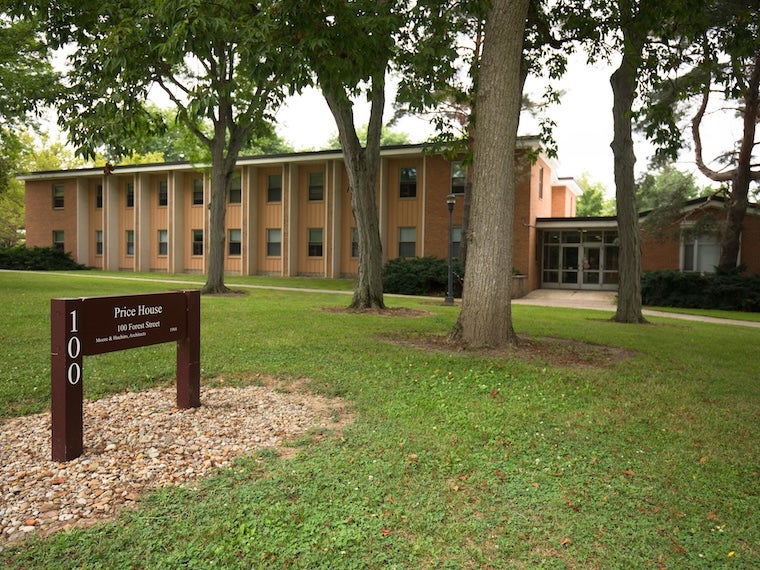 Price House, a two-story brick residence hall surrounded by trees, with a campus sign in the foreground.