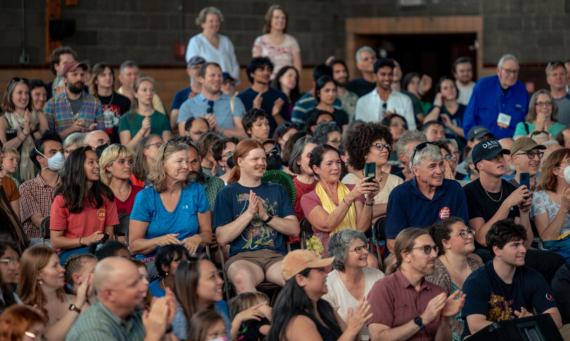 A crowd of people watches an performance that is taking place out of the photo's frame.