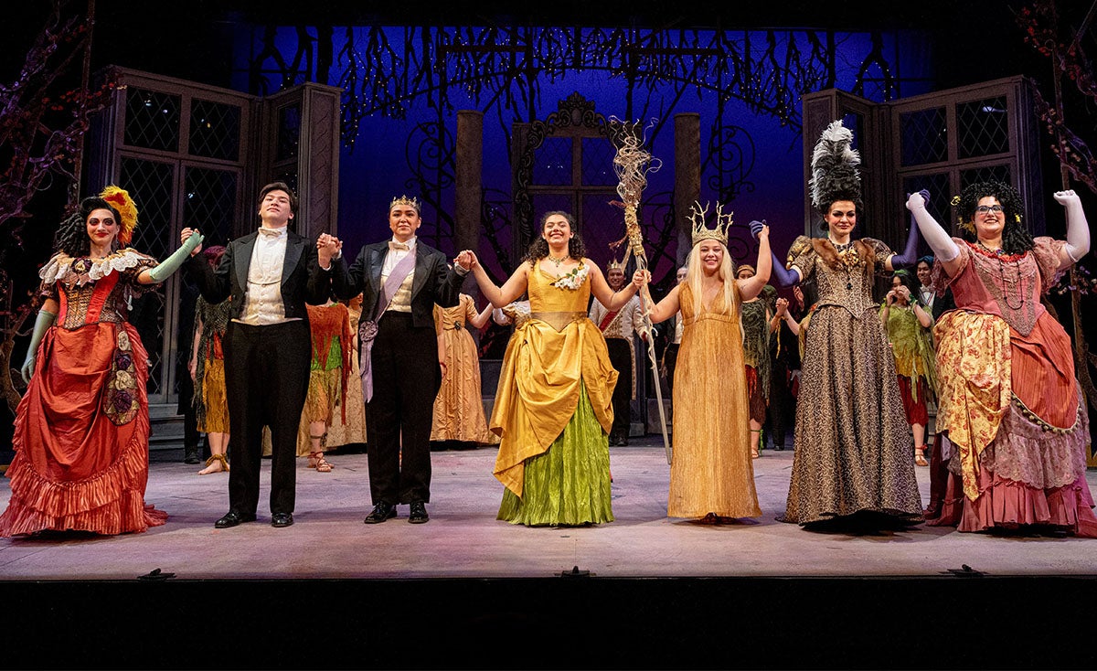 Actors in period costumes taking a bow on stage after a theatrical performance.