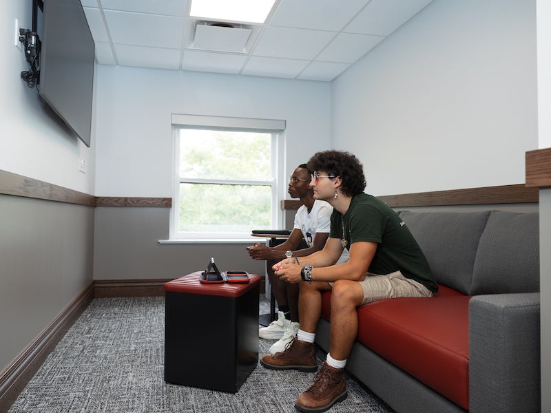 students gaming on a couch in front of a TV screen.