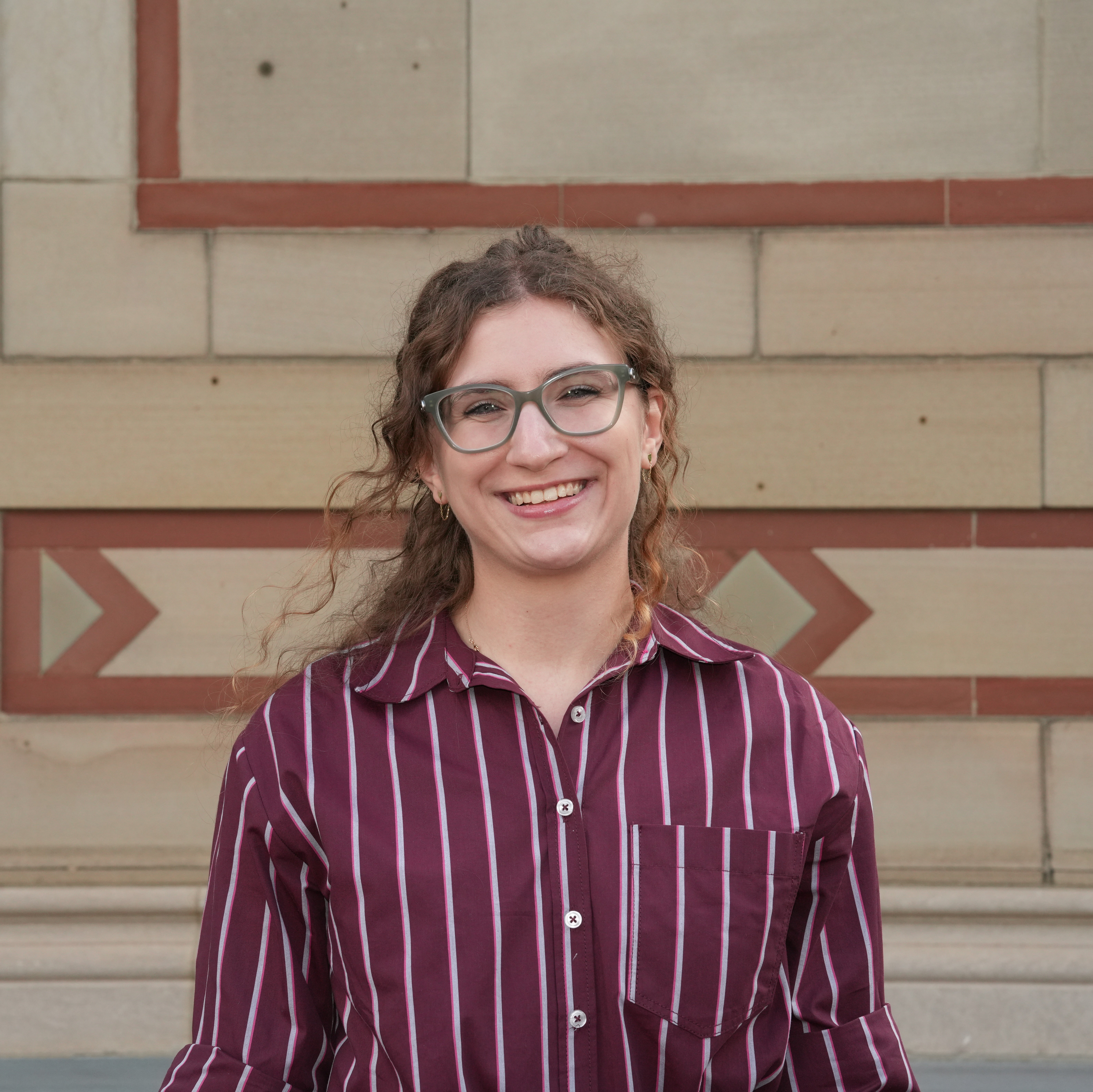 A headshot of a student in a red shirt with curly hair.
