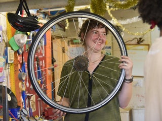A person in a bike shop holds up a wheel.