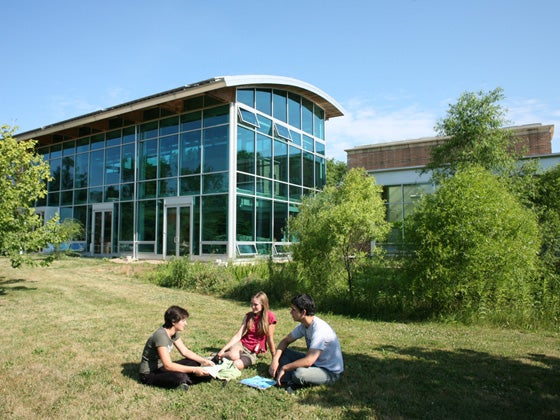 Students sit in a circle in the grass outside the AJLC, a modern glass and brick building.