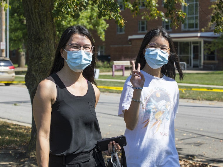 Two masked students walking together on campus.