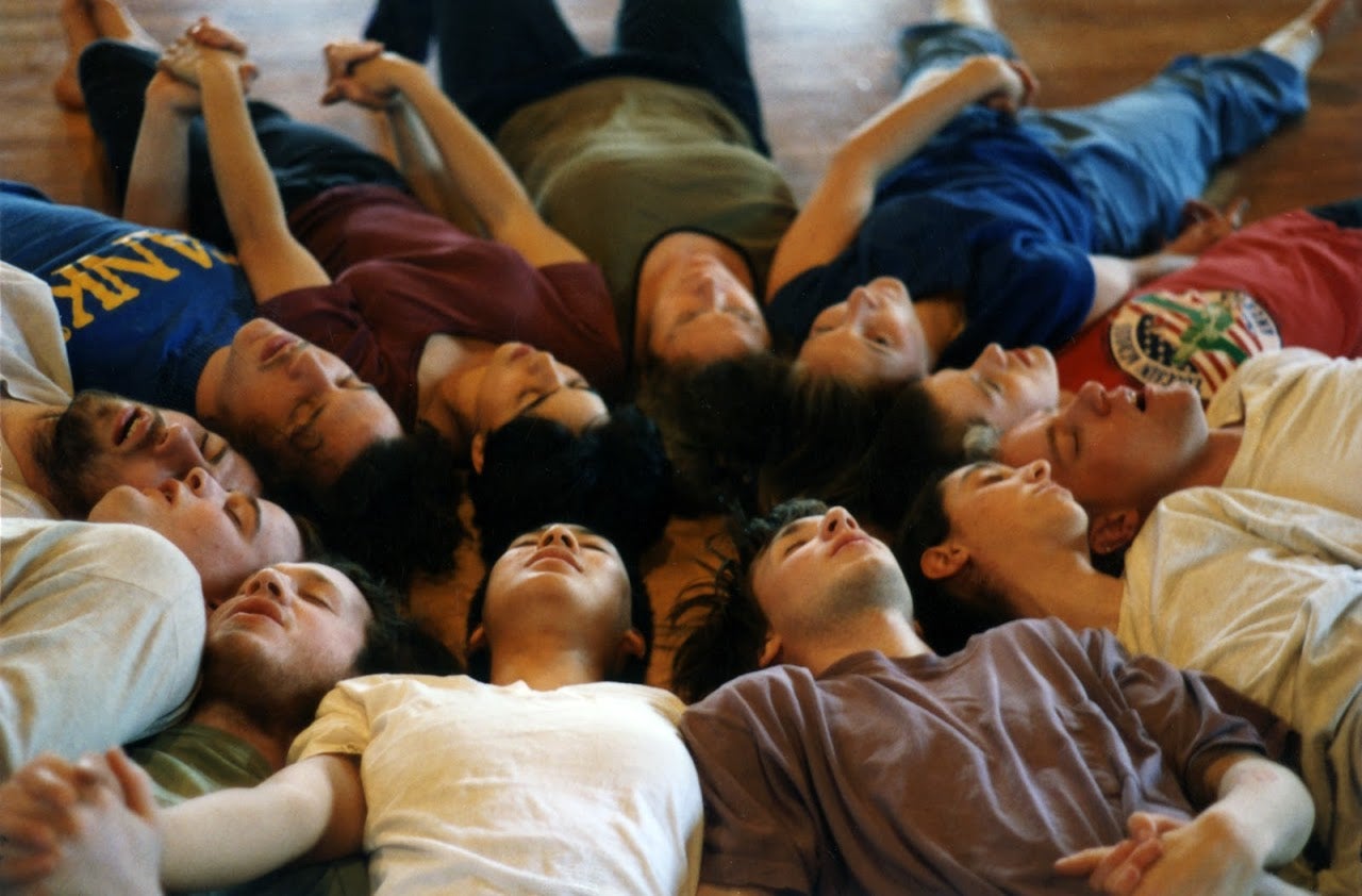 Dancers lying on the floor with their eyes closed and holding hands.