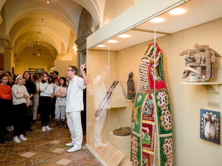 A professor pointing at a glass case of art work while talking to group of students.