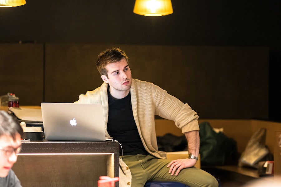 A smartly dressed student with a laptop listens to a presentation.