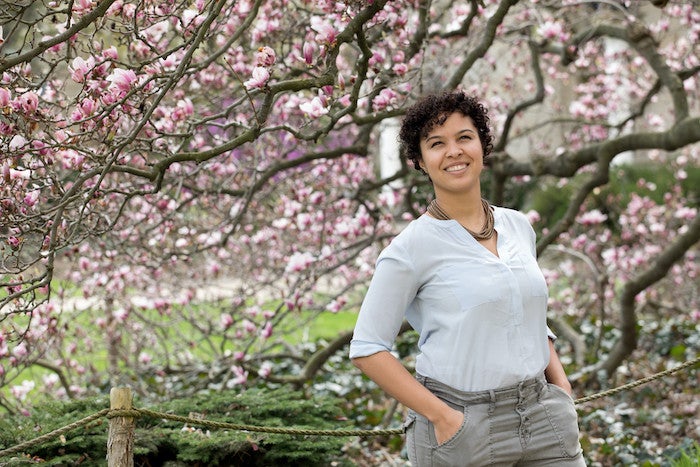 A young woman stands casually by a flowering tree.