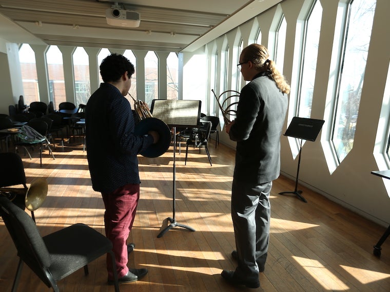 a student takes a horn lesson from a teacher in a large practice room.