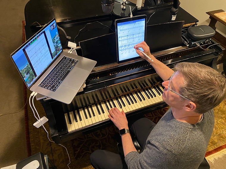 man sitting at the piano with laptop, iPad, and microphone