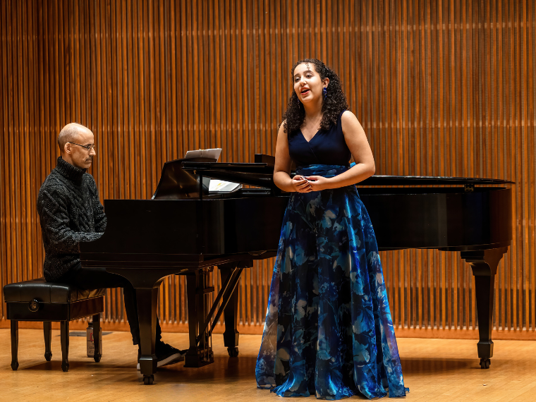 Young female vocalist singing on stage accompanied by man at the piano