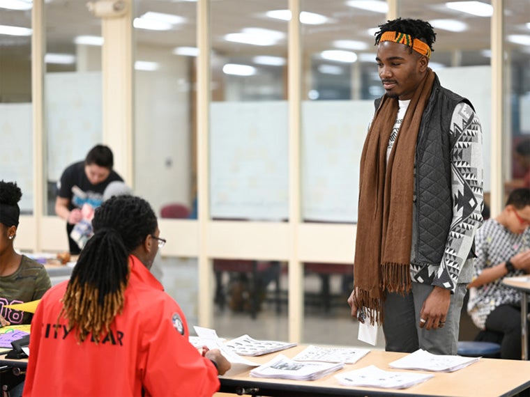 A student approaches a table where someone is giving out fliers.