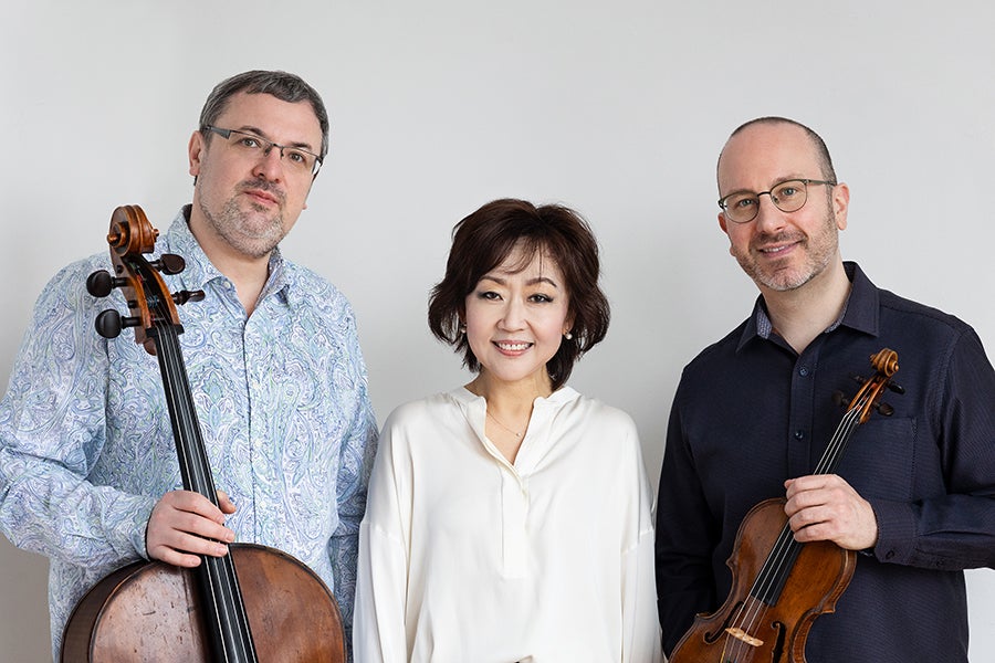 Two men holding stringed instruments with one woman standing between them.
