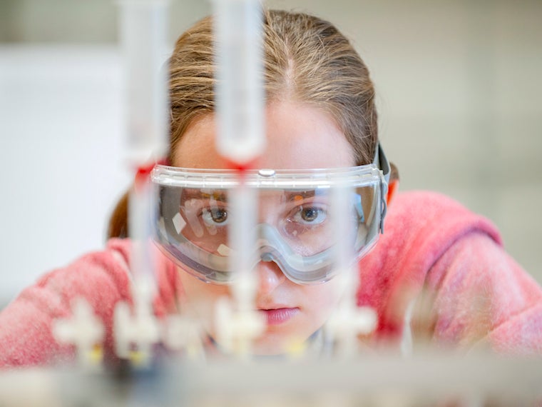 female student with science goggles looking straight at test tubes.