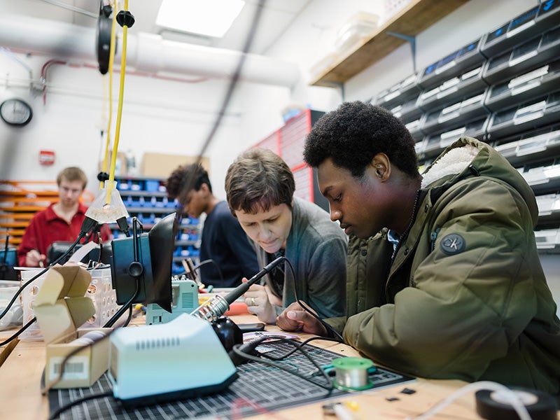 People at a table soldering electronics.