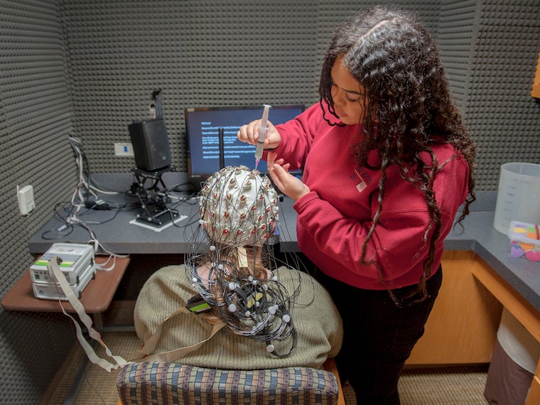 two students on standing placing multisensory nodes on a cap that is on the other student's head.