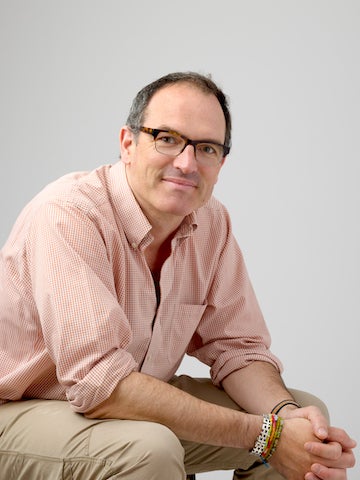 man sitting in chair wearing pink checkered shirt.