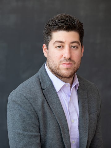 man with dark hair wearing light purple shirt and dark gray jacket posing for portrait.