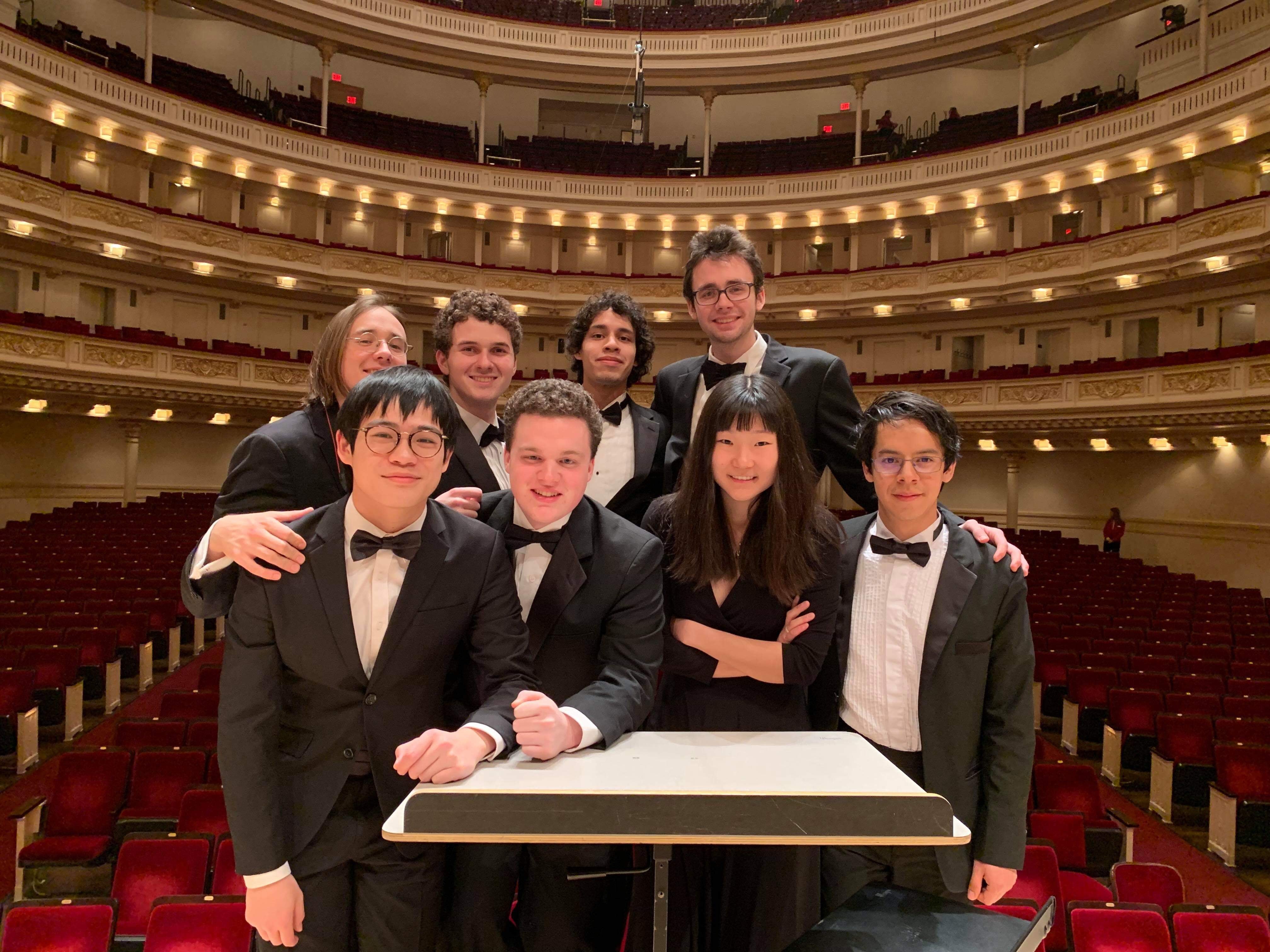 Eight percussionists standing at the conductor's podium in Carnegie Hall.