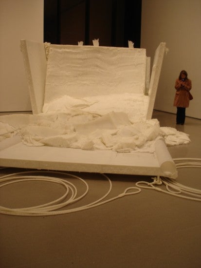 Art museum exhibit: a big white structure, open on one side, with fluffy stuff and a long rope.